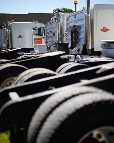 Rows of semi truck chassis are parked in the foreground, with white Yarbrough Transfer Company truck cabs featuring red and yellow logos visible in the background on a sunny day.
